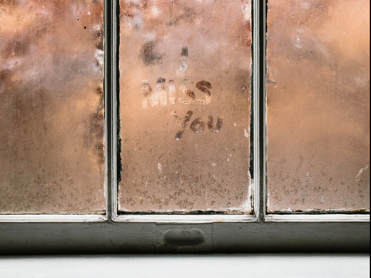 The words "I miss you" are written into the mist condensed on a timber-framed wood.
